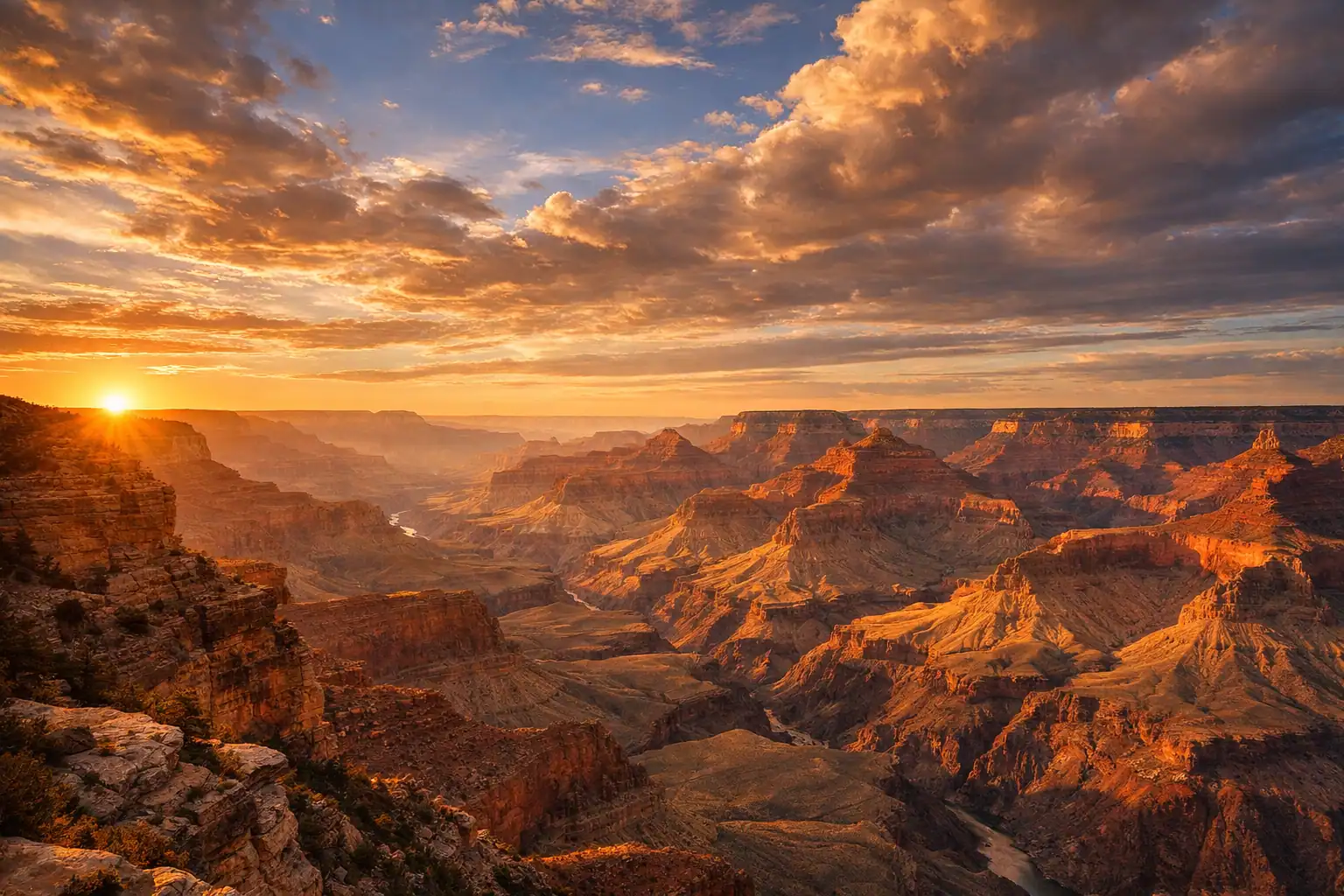Grand Canyon bij zonsopgang vanaf de South Rim, gelaagde rode en oranje rotsformaties tot aan de horizon, dramatische wolken in gouden licht