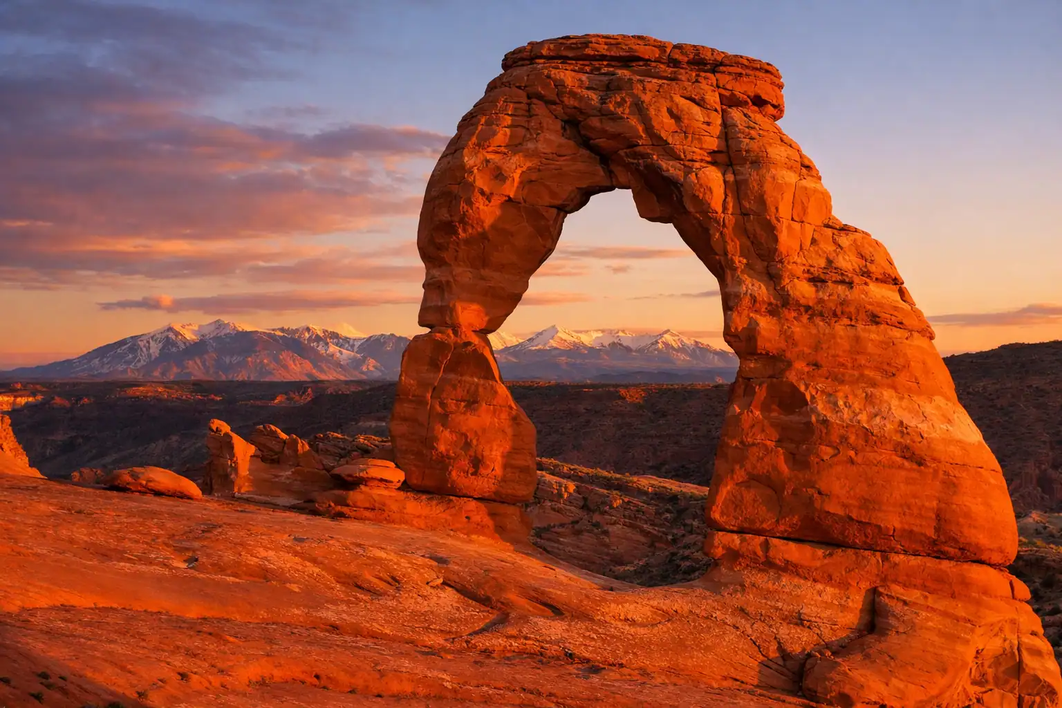 Delicate Arch in Arches National Park bij zonsondergang, de vrijstaande natuurlijke boog met de La Sal Mountains erachter, diep oranje zandsteen