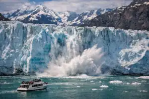 Afkalvende gletsjer in Glacier Bay Alaska met blauwe ijswand, vallende ijsbrokken in turquoise water en tourboot voor schaal