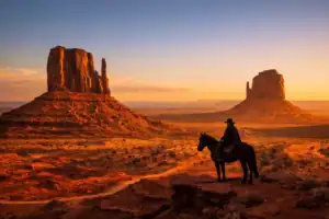 Monument Valley bij gouden uurlicht met iconische buttes en silhouet van Navajo-gids te paard in de rode woestijn